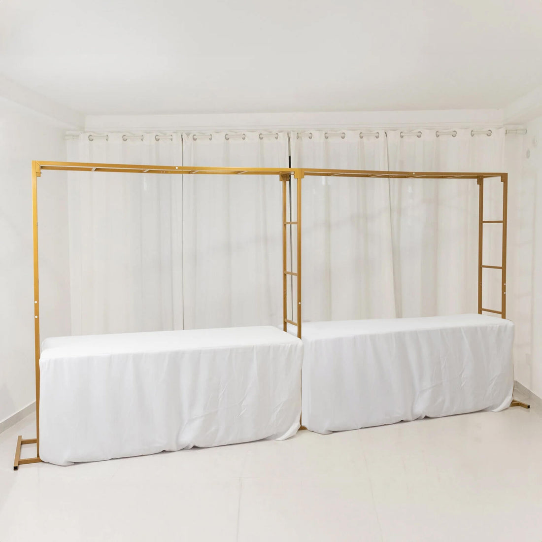 Gold frame display stands with white table covers in a staged setting.