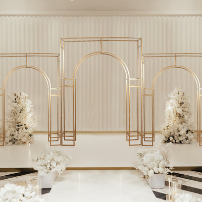Elegant gold archways adorned with white flowers in a stylish event space.