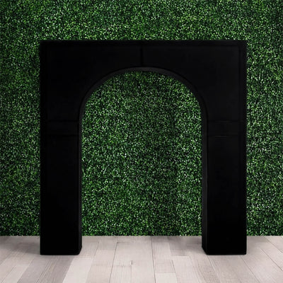 Black arched doorway frame against green hedge wall and light wood floor
