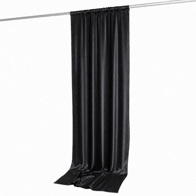 Black satin curtain panel hanging on a rod, long draped fabric backdrop