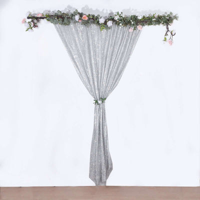 Silver sequin curtain with floral garland on top against a plain white background.
