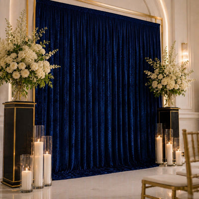 Elegant wedding backdrop with navy velvet drape, white floral arrangements, and candles