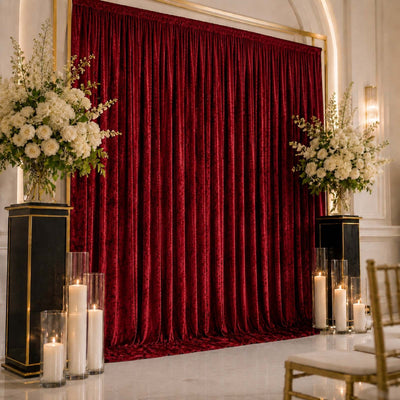 Elegant wedding backdrop with red velvet drapes, white floral arrangements, and candles
