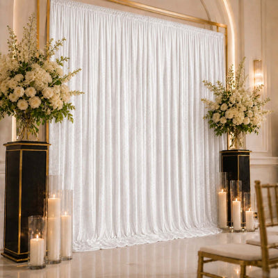 Elegant wedding backdrop with white drapery, floral arrangements, and candles