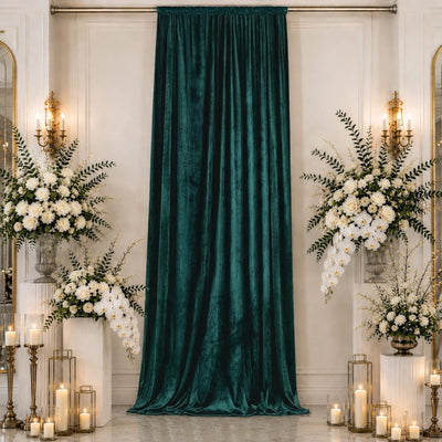 Elegant wedding backdrop with emerald velvet drape, white floral arrangements, and candles