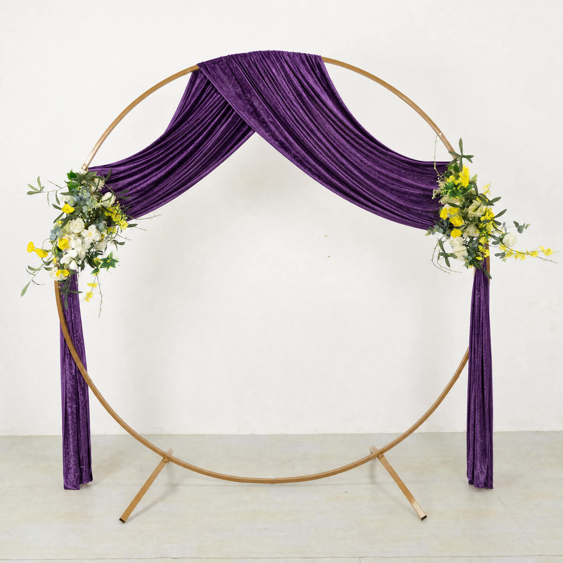 Purple draped round wedding arch with floral accents on gold frame