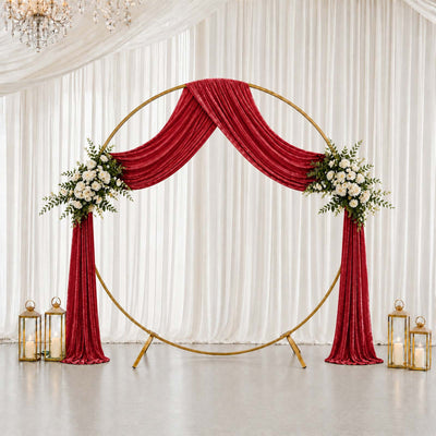 Elegant wedding backdrop with red velvet drapes, gold circle arch, and floral accents