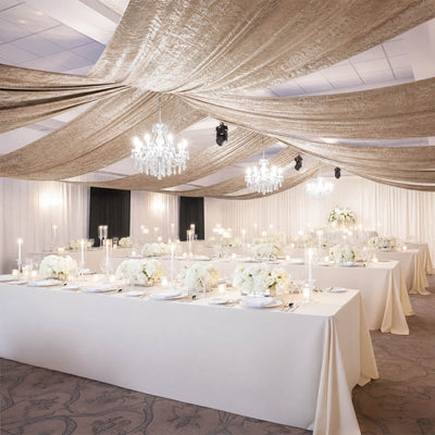 Elegant wedding reception with draped ceiling, chandeliers, and white floral tables