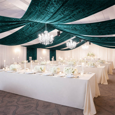 Elegant wedding reception with teal draped ceiling, chandeliers, and white floral tables