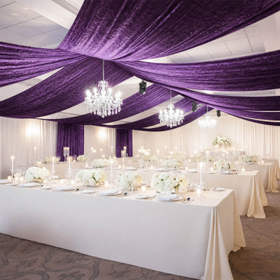 Elegant wedding reception with purple draped ceiling, chandeliers, and white floral tables