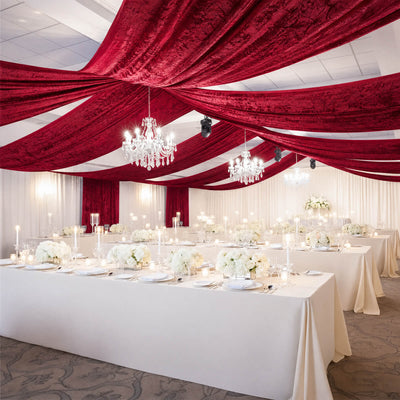 Elegant wedding reception with burgundy draped ceiling, chandeliers, and white tables