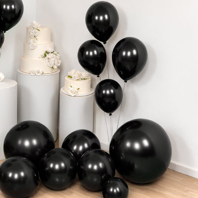 Black balloons in various sizes, arranged with white floral decor and cakes.