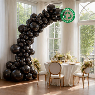 Black biodegradable balloon arch decor in an elegant dining setting with natural light.