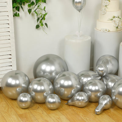 Silver balloons in various sizes scattered on a wooden floor.