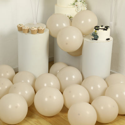 Beige balloons scattered around white cake stands and cupcakes at a celebration.