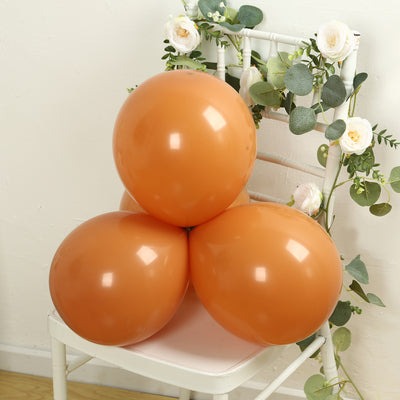 Three orange balloons arranged on a chair with greenery accents.