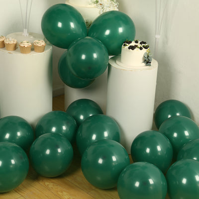 Green balloons scattered around a cake and cupcakes on white pedestals.