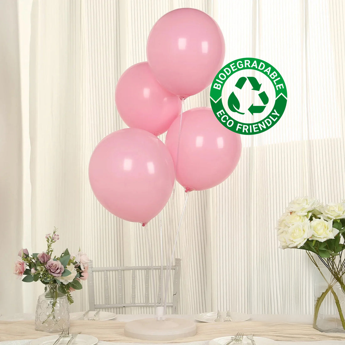 Four pink biodegradable balloons on a table with flowers in the background.