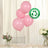 Four pink biodegradable balloons on a table with flowers in the background.