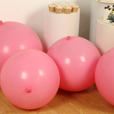 Pink inflatable balloons arranged on a wooden floor with cupcakes in the background.