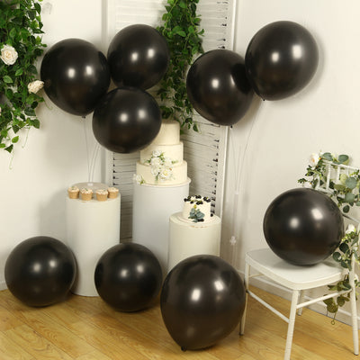 Black balloons with a white cake and cupcakes in a decorated setting.
