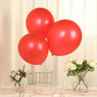 Three red balloons floating above a table with flowers and a light backdrop.
