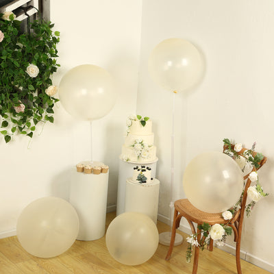 Decorative beige balloons arranged with a cake and flowers in a styled setting.