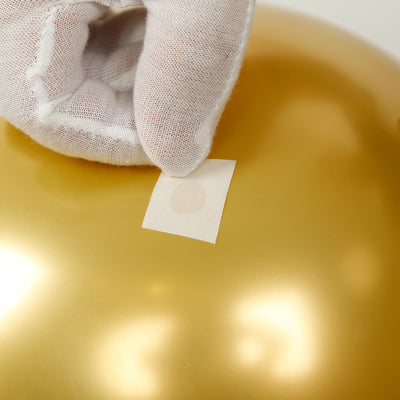 Hand placing a label on a shiny gold surface.