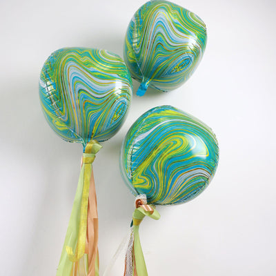 Colorful marbled balloons with ribbons on a plain background