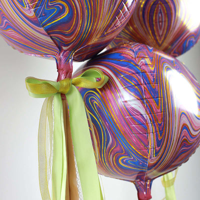 Colorful marbled balloons tied with ribbons, floating against a plain backdrop.