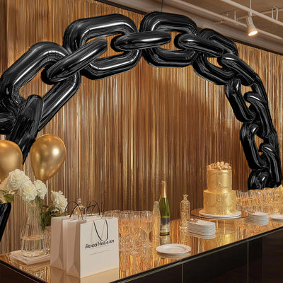 Black balloon chain arch decor at a gold-themed party setup with elegant table settings.