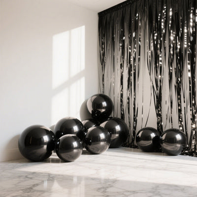 Black balloons clustered near a shimmering black curtain in a bright room.