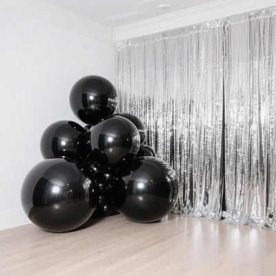 Black balloons clustered in a modern interior with silver foil backdrop.