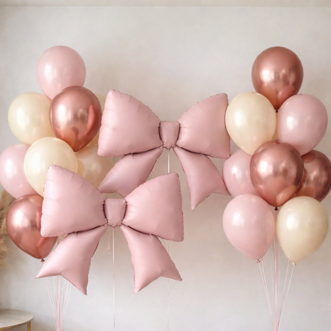 Pink and rose gold balloons with decorative bows for celebrations.