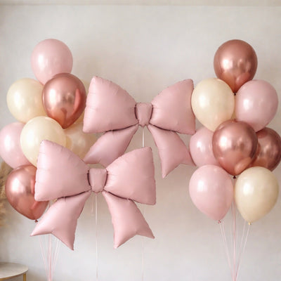 Pink and rose gold balloons with decorative bows for celebrations.