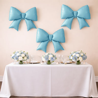 Blue balloon bows and floral centerpieces on a table for a celebration.