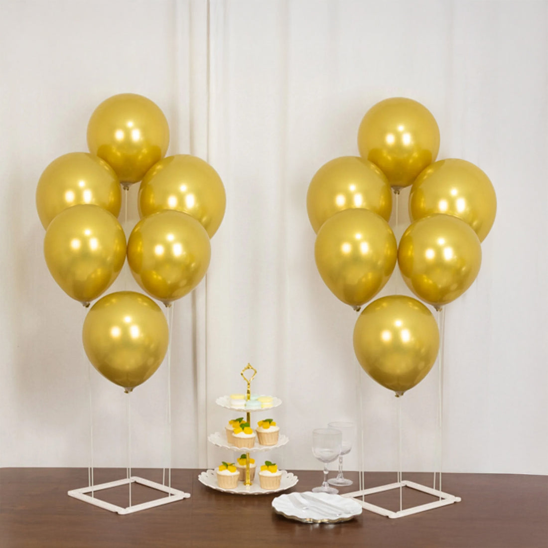 Gold balloons and a dessert stand with cupcakes on a wooden table.