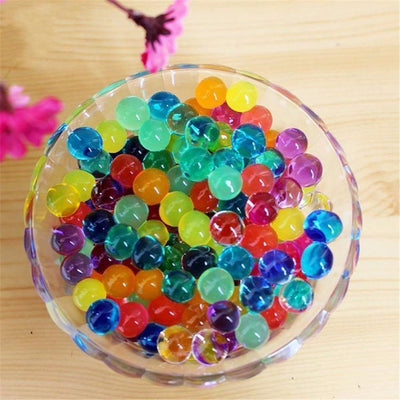 Colorful water beads in a glass bowl on a wooden surface.