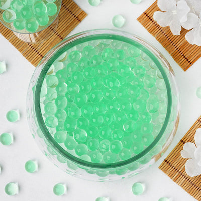 Green water beads in a clear bowl surrounded by decorative elements.