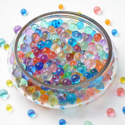 Colorful water beads in a clear bowl with scattered beads around it.