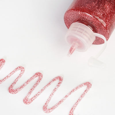 Red glitter glue bottle with a swirl of glitter on a white background