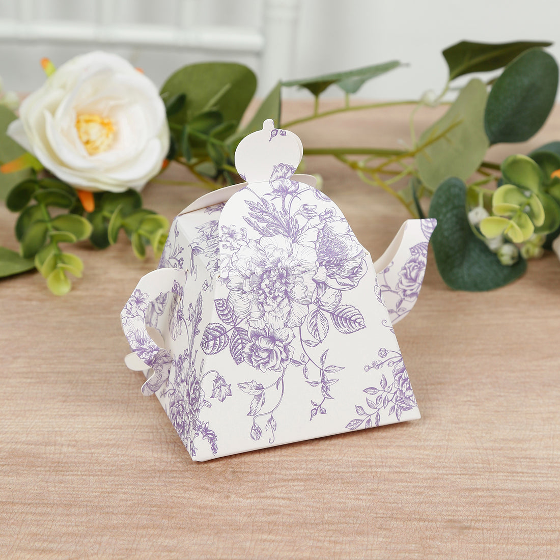 Decorative floral teapot on a wooden surface with greenery