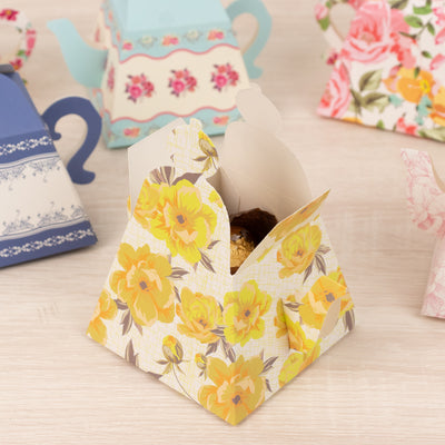 Floral takeout box with a cookie, surrounded by patterned teapots.