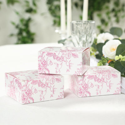 Floral design gift boxes stacked on a table with greenery and candles.