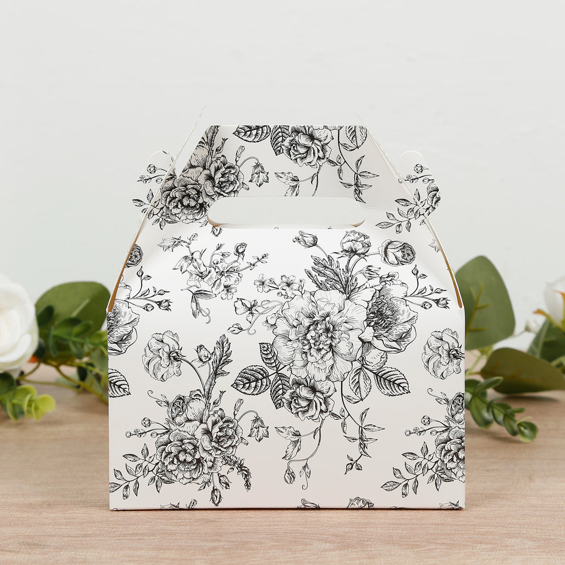 Floral patterned gift box with a handle on a wooden surface.
