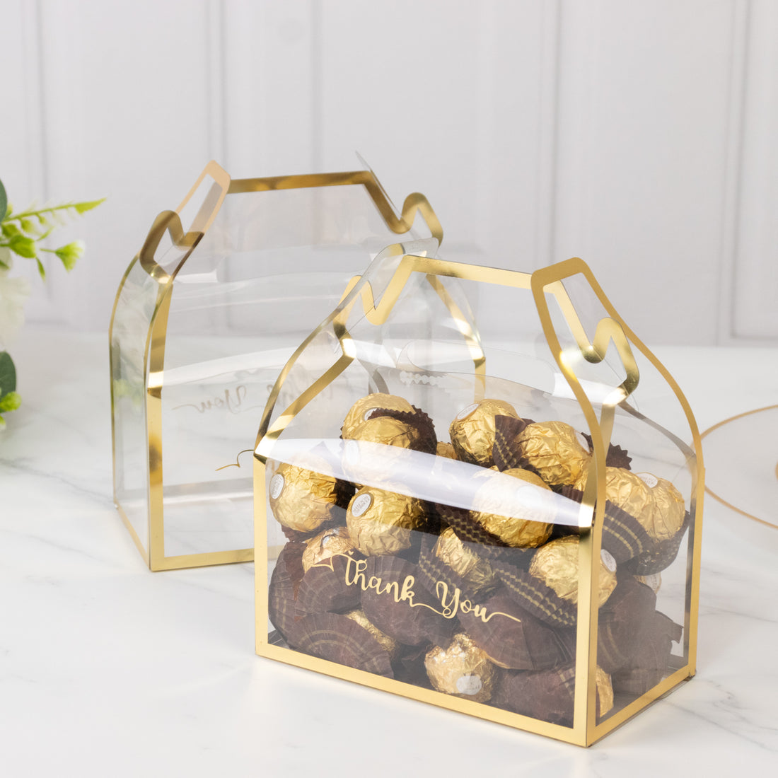 Clear treat boxes with gold trim filled with assorted chocolates.