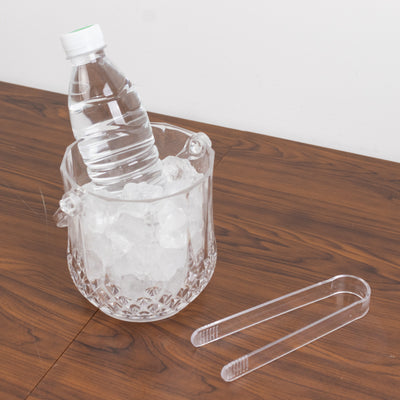 Clear ice bucket with a water bottle and tongs on a wooden surface.