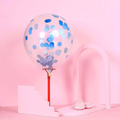 Clear balloon with blue confetti on a stand, pink backdrop with macarons and arch.