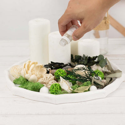 Hand adding essential oil to a decorative tray with candles and natural elements.
