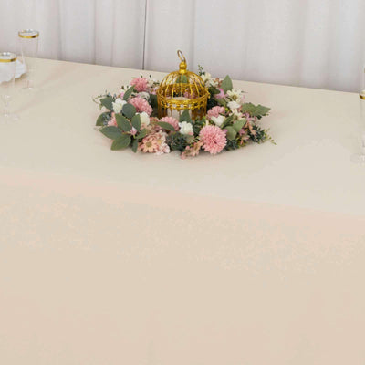 Golden birdcage centerpiece surrounded by pink flowers on a table.